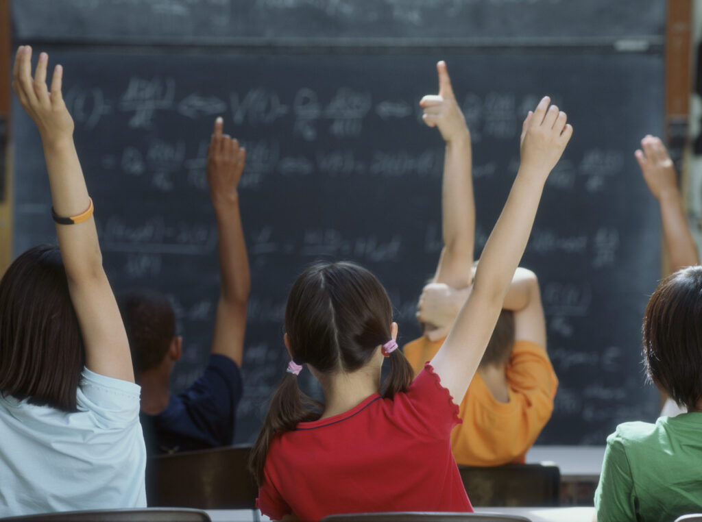 Rear view of class raising hands --- Image by © Royalty-Free/Corbis