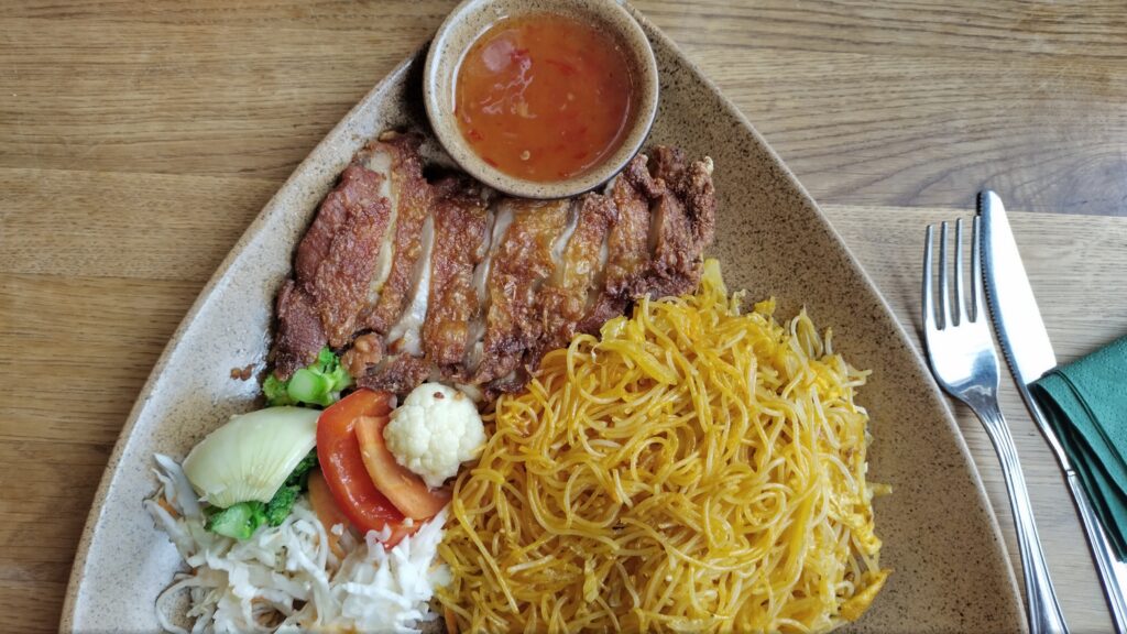 A képen egy tál vietnámi étel látható, sült-bundázott kacsamellek szeletelve zöldség és rízstészta körettel.